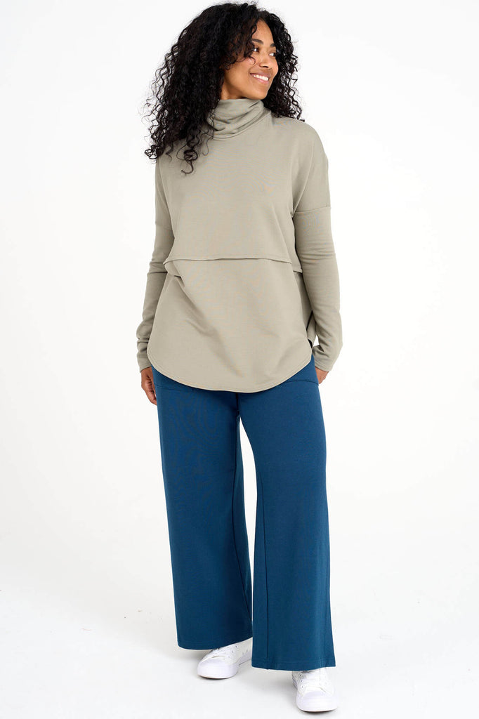 Woman wearing eucalyptus green Tencel oversized Abigail turtleneck with blue palazzo pants, made by Canadian loungewear label Advika. 