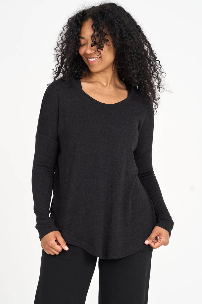 Woman wearing black Tencel scoopneck long sleeve top with split back hem, made by Canadian loungewear label Advika. 