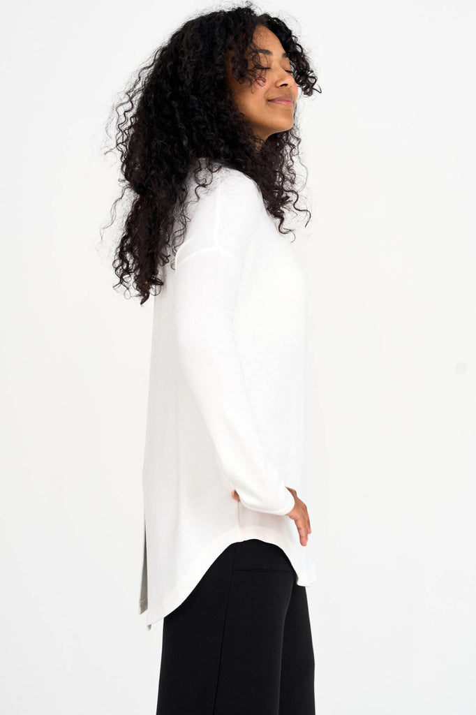 Side view of woman wearing ivory Tencel scoopneck long sleeve top with split back hem, made by Canadian loungewear label Advika. 