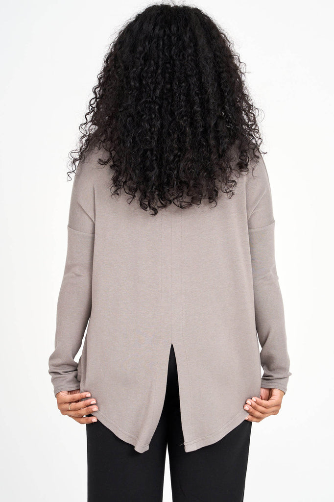 Back view of woman wearing ming beige grey Tencel scoopneck long sleeve top with split back hem, made by Canadian loungewear label Advika. 