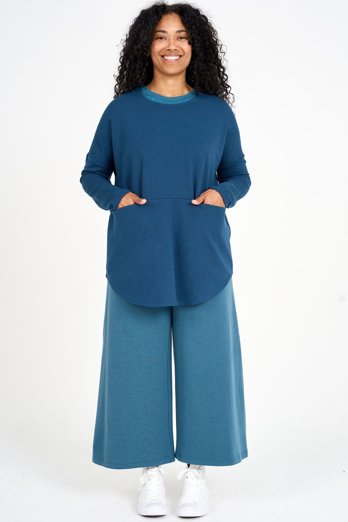 Woman wearing bluebell blue Tencel oversized long sleeve top with large front in-seam pockets and teal palazzo pants, made by Canadian loungewear label Advika. 