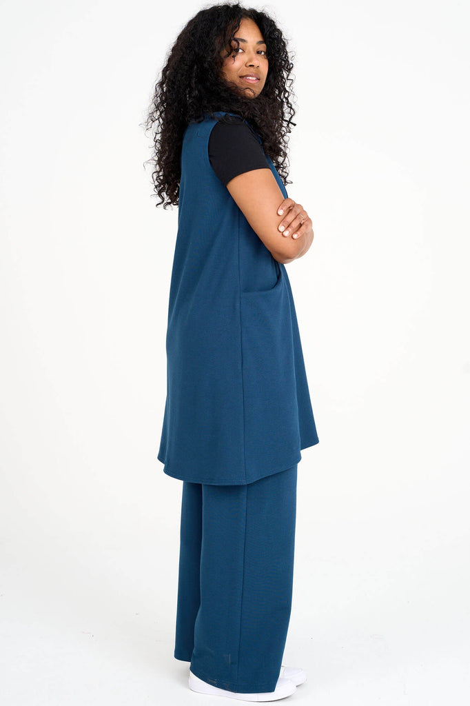 Side view of woman wearing bleubell blue Tencel tunic dress over black t-shirt and blue palazzo pants, made by Canadian loungewear label Advika.