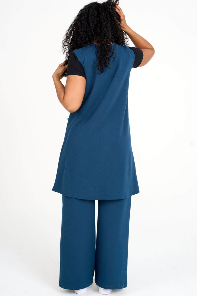 Back view of woman wearing bleubell blue Tencel tunic dress over black t-shirt and blue palazzo pants, made by Canadian loungewear label Advika.