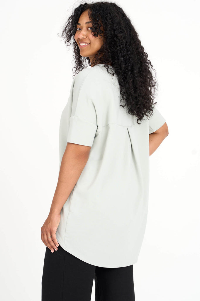 Back view of woman wearing light sage green Tencel short sleeve slouchy top with back pleat detail, made by Canadian loungewear label Advika. 