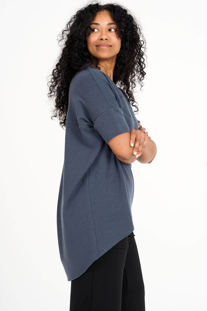 Side view of woman wearing steel blue Tencel short sleeve slouchy top with back pleat detail, made by Canadian loungewear label Advika. 
