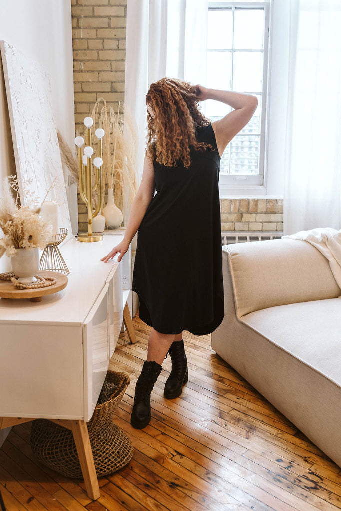 Woman wearing Tencel scooped hem dress in black, Canadian made women's loungewear, standing in living room